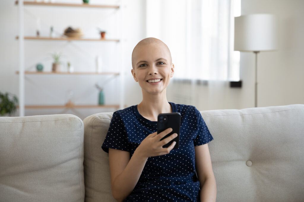 A woman with cancer sits on a couch holding her cellphone.